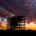 Silhouette of a commercial building under construction with a crane against a dramatic sunset sky.