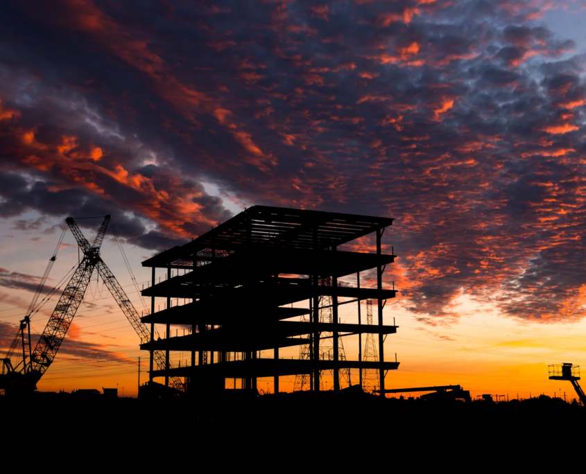 Silhouette of a commercial building under construction with a crane against a dramatic sunset sky.